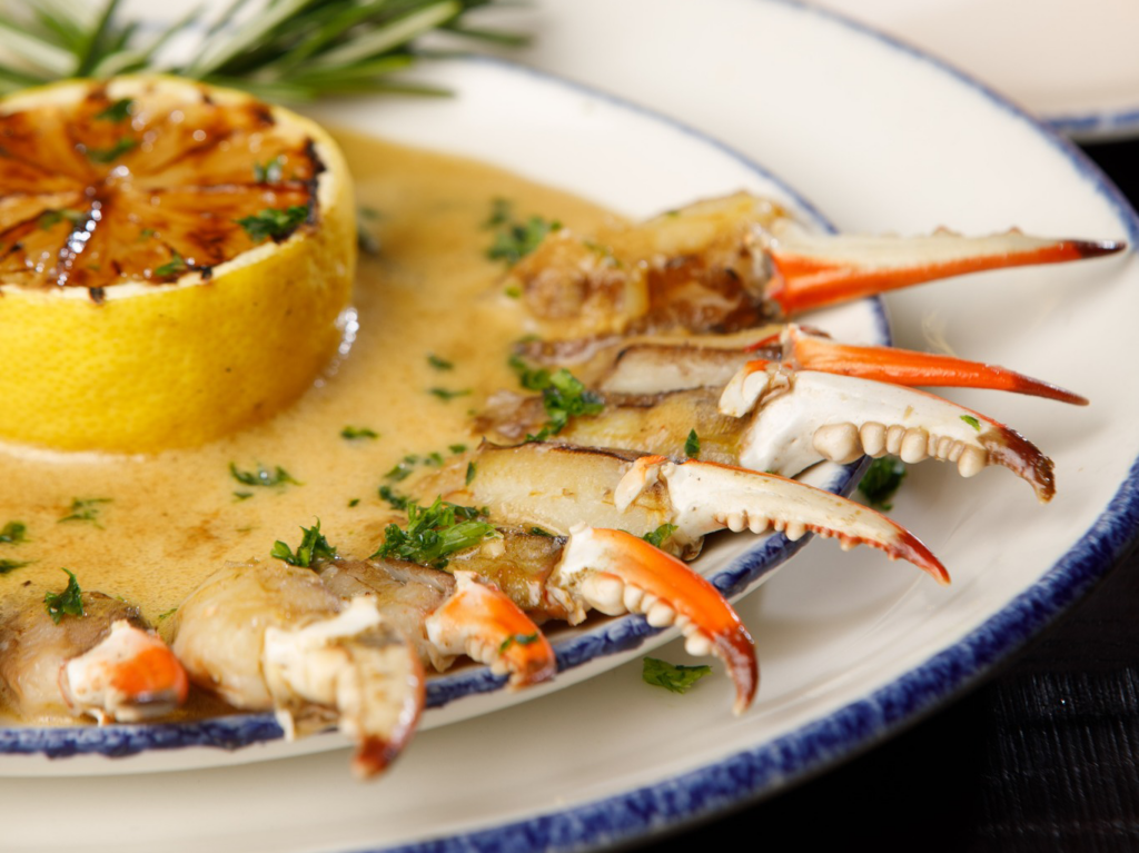 Crab claws in a creamy sauce, garnished with herbs and a grilled lemon slice, showcase the flavors of a Louisiana seafood restaurant.