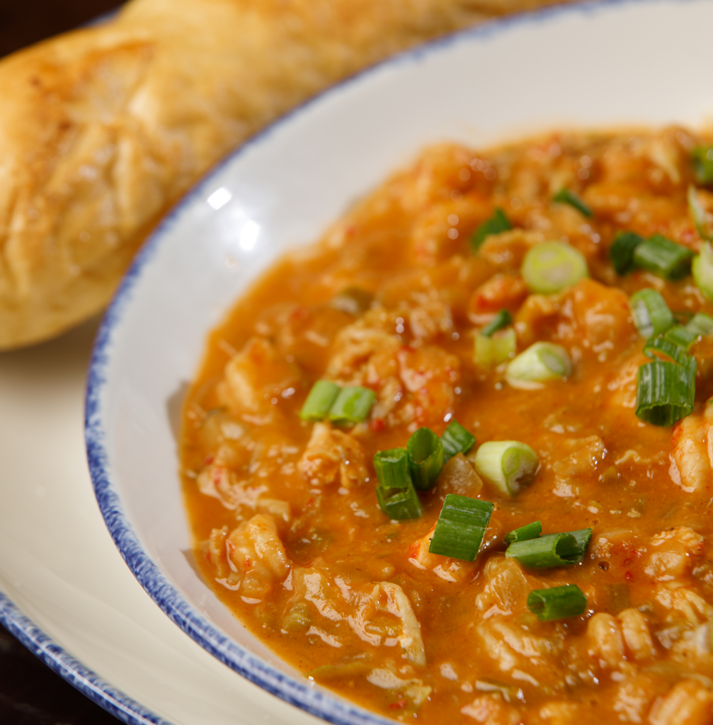 A bowl of seafood bisque topped with chopped green onions, served with a French baguette, perfect for enjoying Louisiana cuisine.