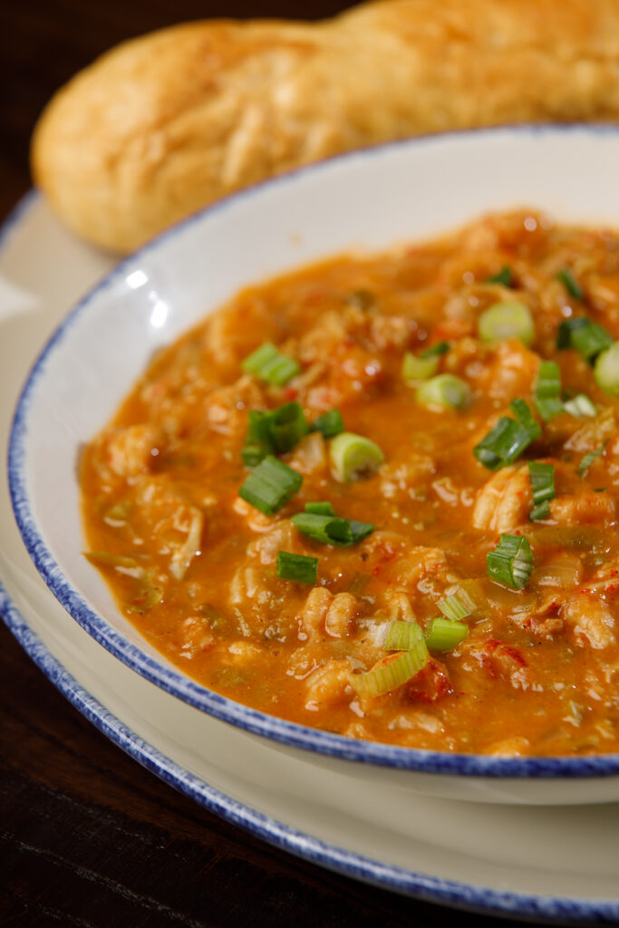 A plate of gumbo garnished with chopped green onions at a Louisiana seafood restaurant. Crusty bread sits on a white plate with a blue rim.